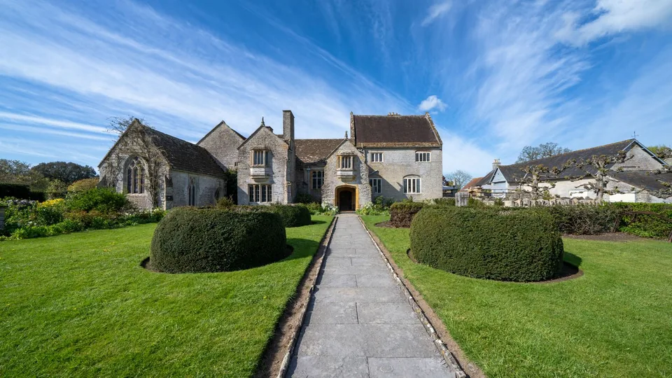 A historic stone house with formal gardens and a lawn.