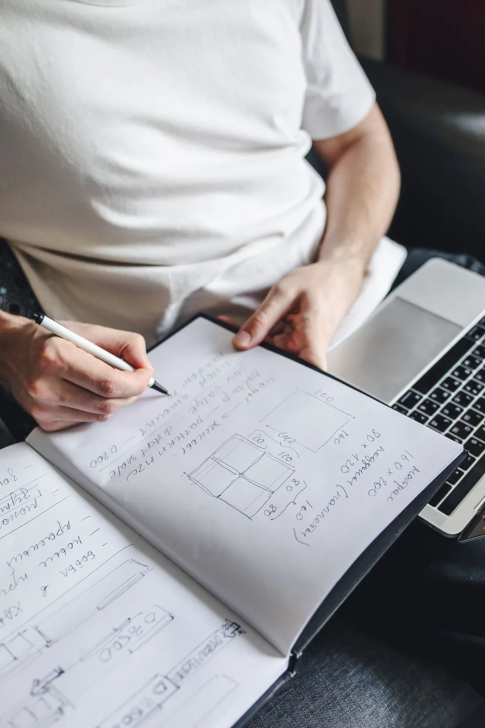 A person writing notes beside a laptop.