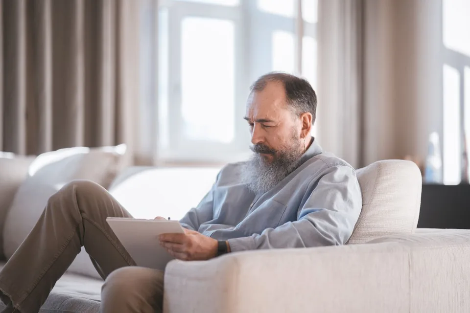 A man reading information on a tablet while sitting on a sofa.
