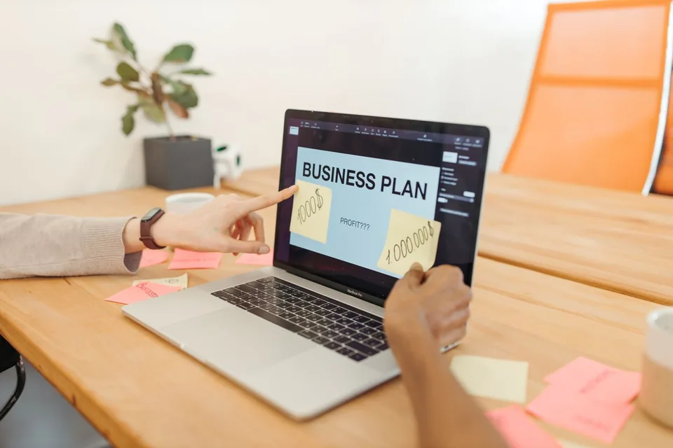 A laptop displaying a business plan beside a notebook.