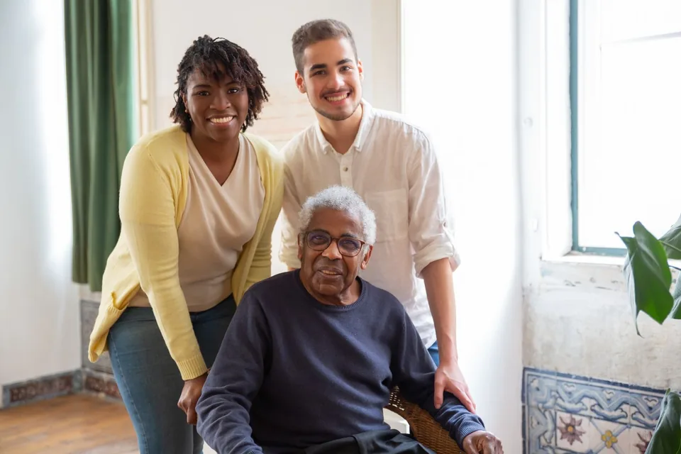 Three adults smiling together in a home setting.