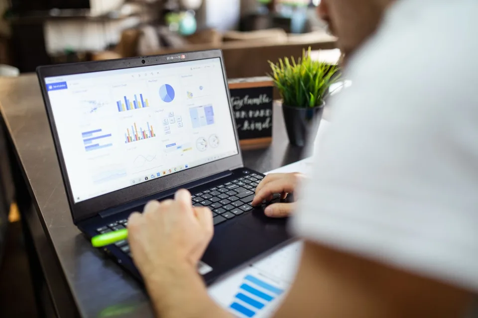 A person reviewing charts and reports on a laptop.